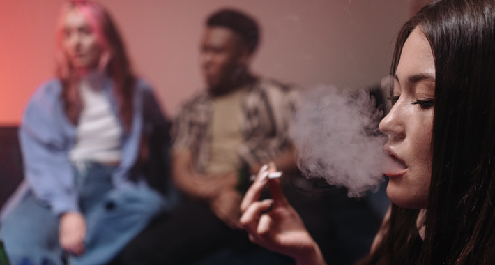 Jeune femme fumant du cannabis dans un milieu intérieur, entourée de deux personnes
